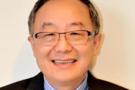 Image of Xiao-Fan Wang, man with dark and grey hair wearing glasses, a blue and white striped shirt, tie and dark jacket